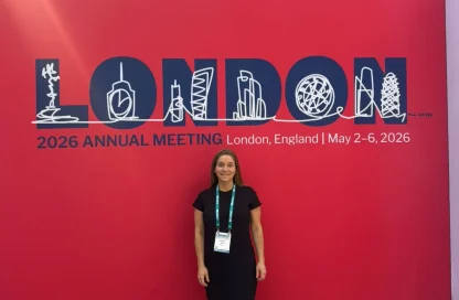 Woman in a black dress standing in front of a red INTA London 2026 banner and conference badge visible around her neck