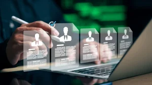 Person using a stylus to interact with floating resume cards on a laptop screen, showing silhouettes of professionals.