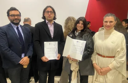Four people pose for a photo at an award ceremony; two men hold certificates while two women smile beside them.
