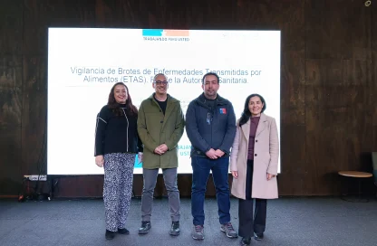 Four people stand together on a stage in front of a bright screen with Spanish text. They smile at the camera, posing for a group photo.