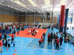 Indoor gymnasium full of people, including children, engaging in various activities on blue and orange courts.