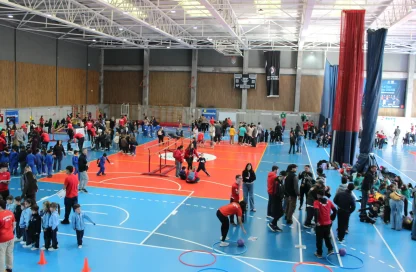 Indoor gymnasium full of people, including children, engaging in various activities on blue and orange courts.