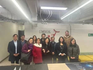 Group of eleven people posing together in a coworking space, smiling at the camera, with a 'COWORKING' sign and modern, exposed-ceiling interior behind them.