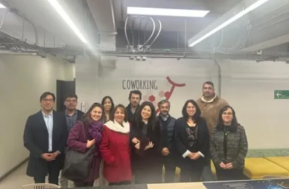 Group of eleven people posing together in a coworking space, smiling at the camera, with a 'COWORKING' sign and modern, exposed-ceiling interior behind them.