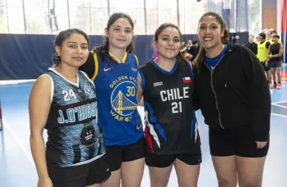 Four female basketball players pose together on an indoor court, smiling for the camera in their team uniforms.
