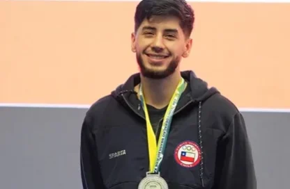 Smiling young man in a black zip-up jacket with a circular patch, wearing a yellow-lanyard with a silver medal around his neck.